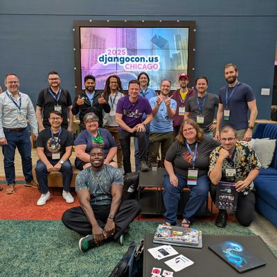 A group of smiling people in a hotel lobby beneath a giant screen that says DjangoConUS 2025.