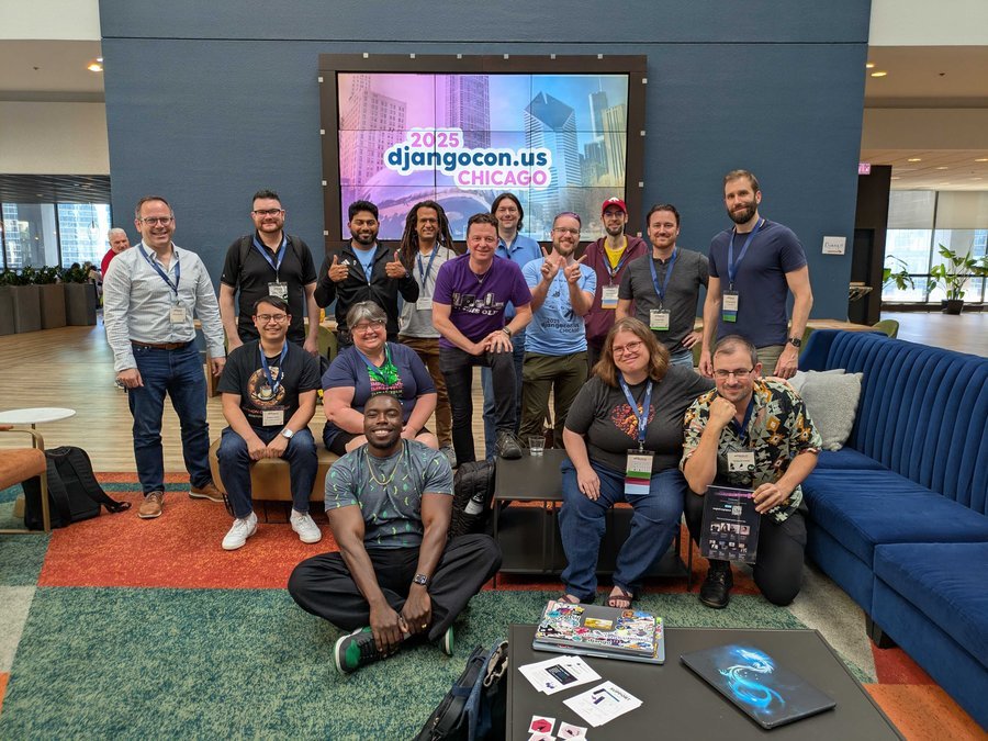 A group of smiling people in a hotel lobby beneath a giant screen that says DjangoConUS 2025.