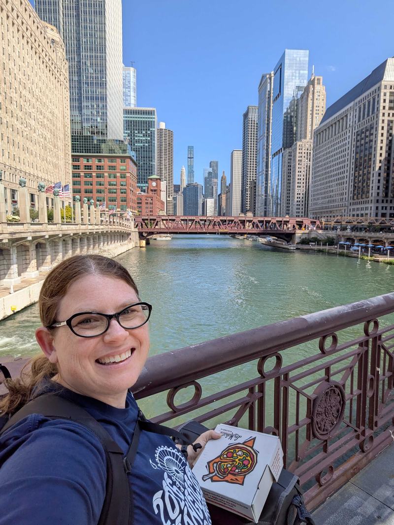 Meagen Voss smiling for a selfie by the Chicago River holding a Lou Malnati's pizza box.