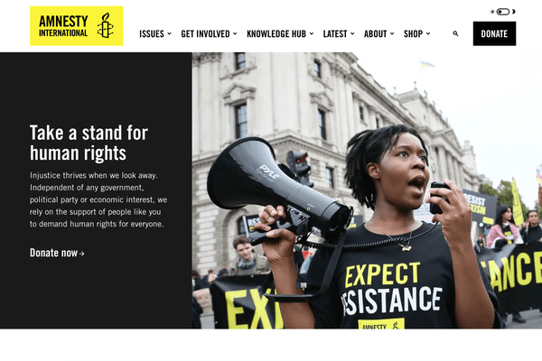 A view of the home page for Amnesty International UK with their logo, menu, and a story with a picture of a black woman holding a megaphone.
