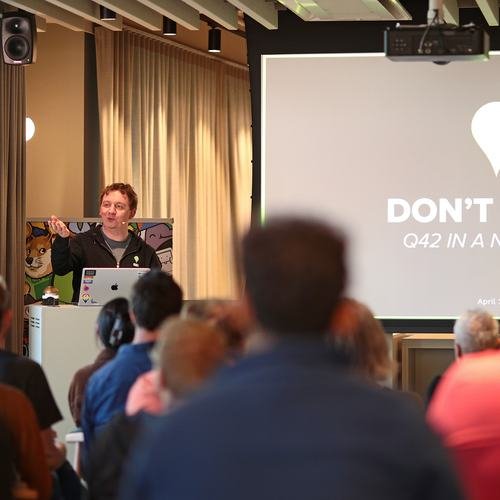 A speaker giving a talk behind a podium to a full audience at the Q42 office.