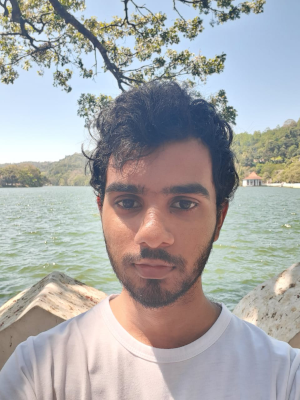 This is a photo of Sandil Ranisinghe outside on a sunny day with some lovely waves and trees behind him.