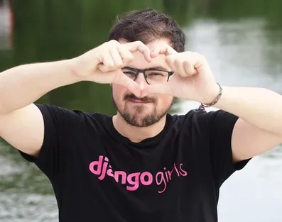Thibaud Colas making a heart shape with his fingers in front of his face while wearing a Django Girls t-shirt.