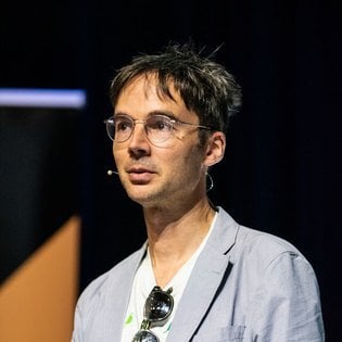 Tom Dyson wearing a suit and a microphone, speaking behind a podium.