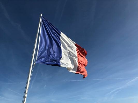 The flag of France on a flagpole flapping in the wind. Photo by Anthony Choren on Unsplash, available at https://unsplash.com/@tony_cm__