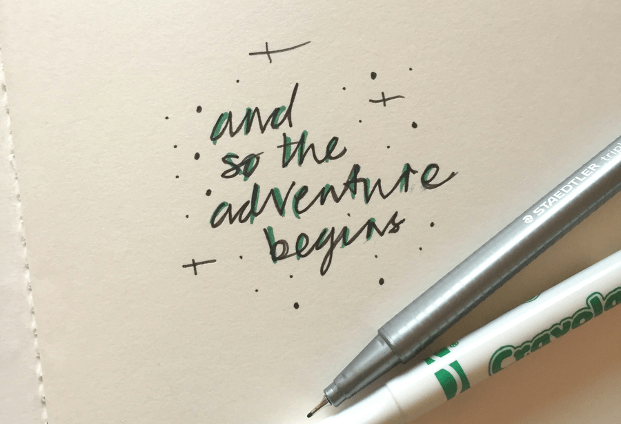 A piece of paper that has the words and so the adventure begins written in green ink. There is a pen and a green crayola marker be beneath the words.