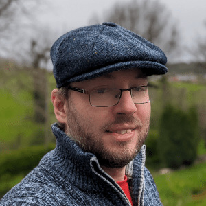 Tom Usher standing outside in the English countryside with a hat and jumper on.